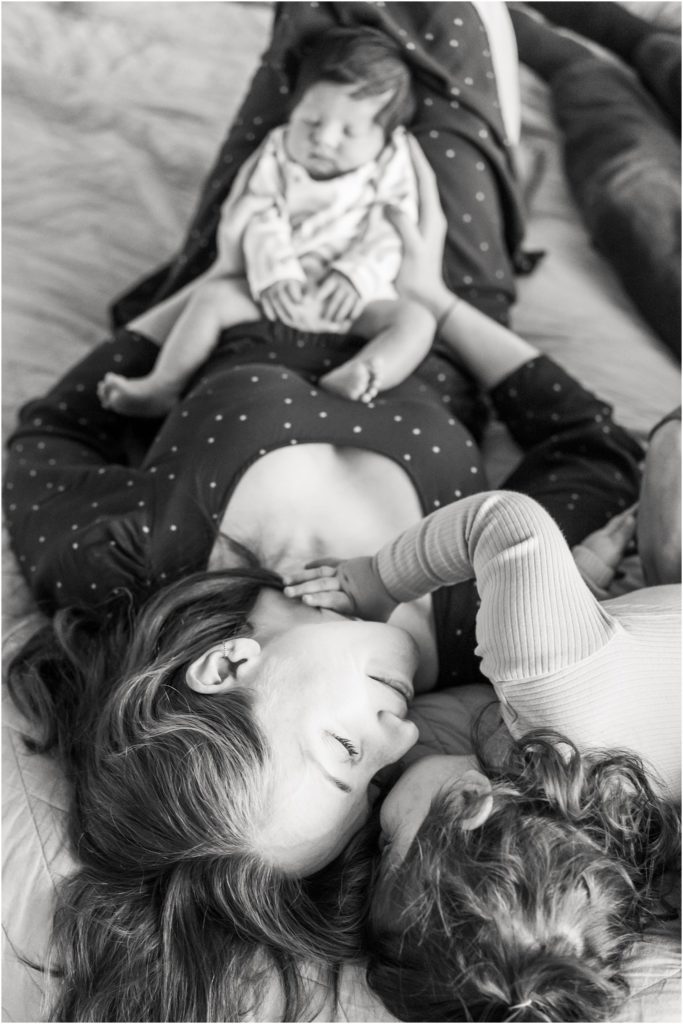 newborn photos in charlottesville with sibling and mom laying on the bed holding baby